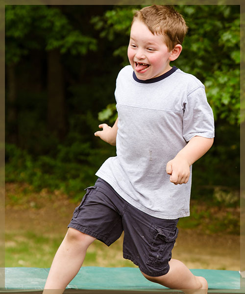 Young boy running around trampoline with tongue out