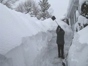 man shoveling a path through snow with piles over his head on both sides
