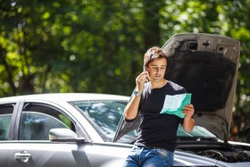 Man on phone looking at piece of paper with car hood propped open