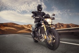 Man riding motorcycle on highway with mountains behind him