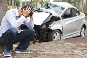 Man with head in hands in front of smashed car from accident