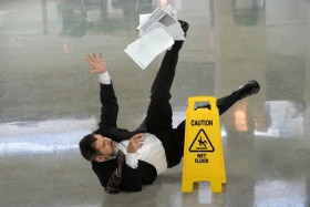 Man slipping on wet floor next to caution sign