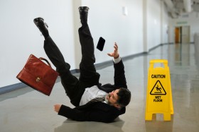 Businessman slipping on wet floor and losing briefcase and cell phone next to caution sign
