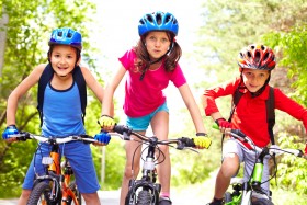 Three children on bikes wearing helmets and biking gloves