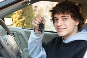 Teenage boy holding up car keys sitting in driver's seat