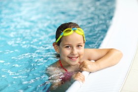 Girl with yellow swim goggles on her head in a swimming pool