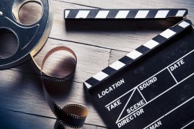 Director's clapboard and movie reel laying on wood