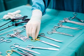 Tray of surgical tools laid out as gloved hand reaches for suture scissors
