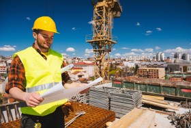 Construction worker with hardhat on looking at blueprint standing on top of building