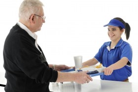 Teen worker handing tray of food to elderly man