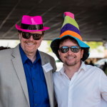 Two men smiling with sunglasses and colorful hats on