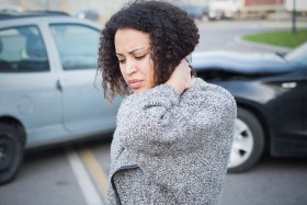 Woman holding neck painfully while standing in front of fender bender accident