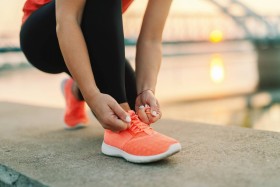 Woman tying coral colored running shoe