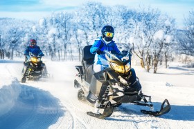 Two people riding on snowmobiles on a snowy trail