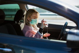 Woman in car with mask on while applying hand sanitizer