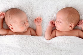 Newborn twin babies laying on white blanket.