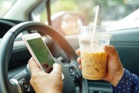 Person driving while using a cell phone and holding a cup of coffee.
