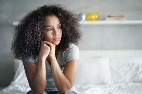 Woman sitting on a bed looking sad.