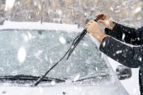 Person adjusting windshield wiper blade on a snowy day.