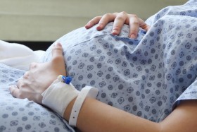 Pregnant woman in hospital gown with hand on stomach.