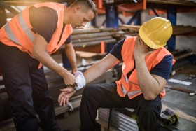 A worker helps an injured coworker with a bandage on their wrist.