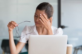 Woman with a headache sits in front of a computer.