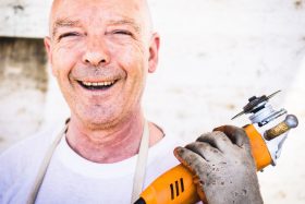 A smiling older worker holding a power tool.