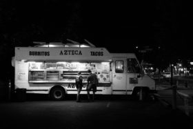 Black and white photo of a food truck with two people standing in front of it.
