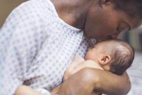 A mother in a hospital gown kisses the head of a newborn baby.