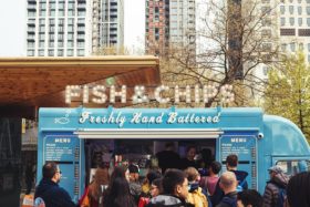 A crowd gathered in front of a food truck selling fish and chips.