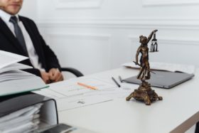 A lawyer sits behind a desk with papers and a Lady Justice statue on it.