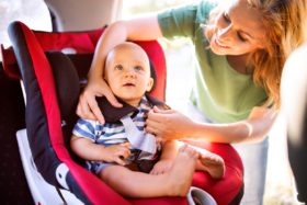 A mother buckles her baby into a car seat.