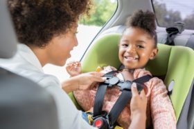 A parent adjusts the straps on a car seat while the child smiles.