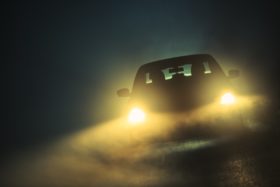 A car's headlights seen driving on a foggy night.