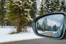 The side mirror of a car being driven on a snowy road.