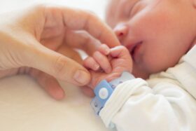 A woman's hand holds the hand of a sleeping baby wearing a hospital bracelet.