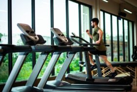 A row of treadmills facing a window with a man running on one of them.